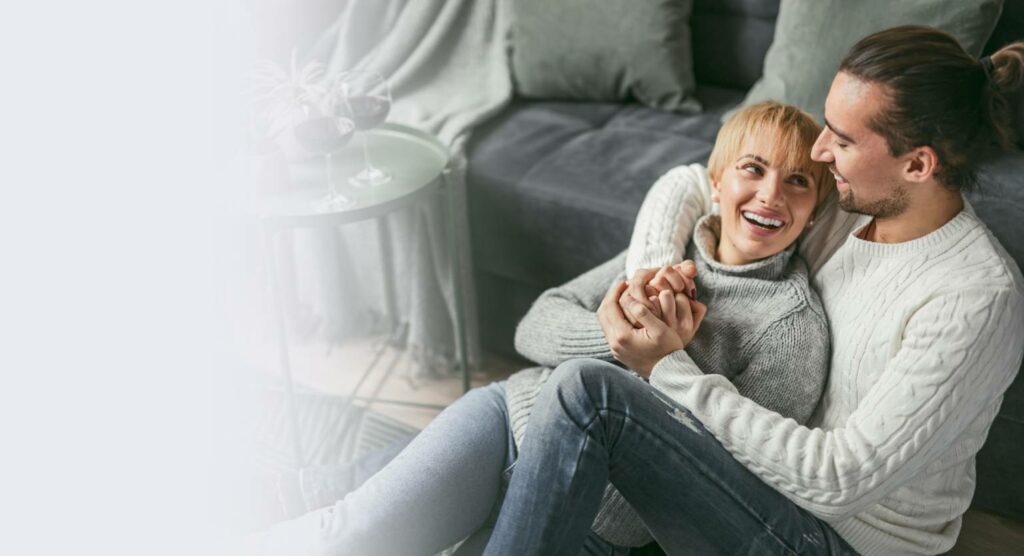 Couple smiling and holding hands while sitting on the floor in a cozy home setting