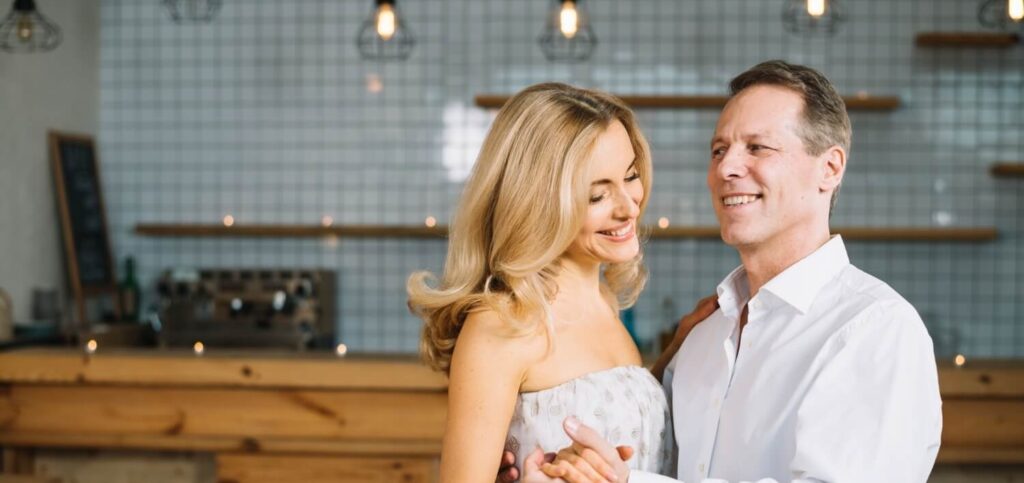 Middle-aged couple smiling and dancing together in a warmly lit indoor space