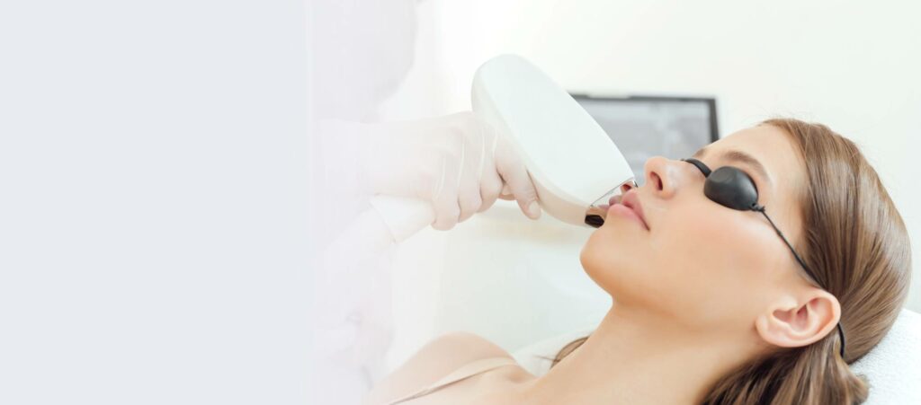 Woman undergoing laser facial treatment while lying down with protective eye goggles