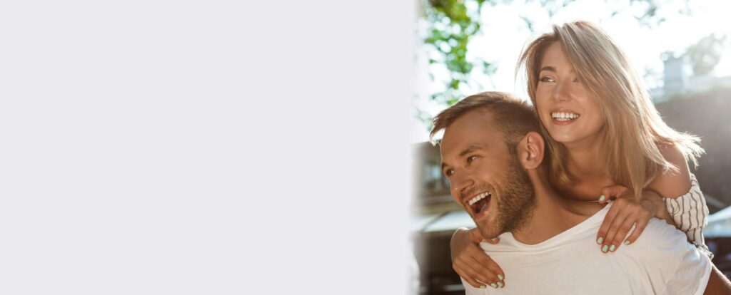 A couple smiling and laughing together outdoors, with the woman on the man's back
