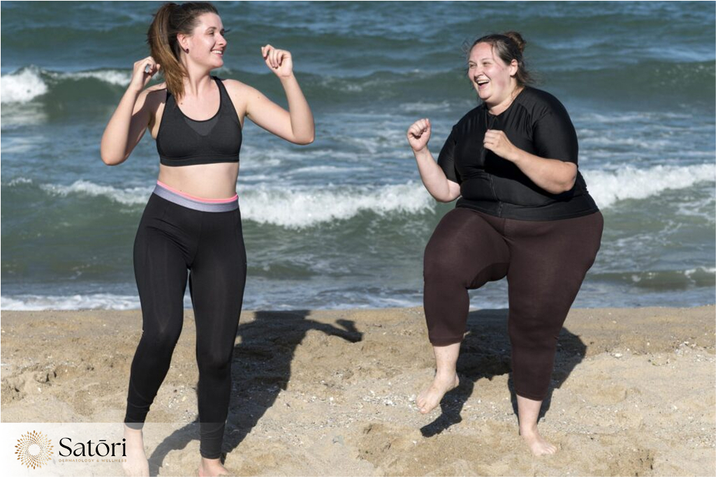Fit woman and obese woman working out together on the beach, promoting body positivity and fitness