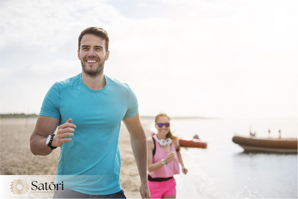 Happy couple running along the beach shoreline during sunrise for fitness and wellness.