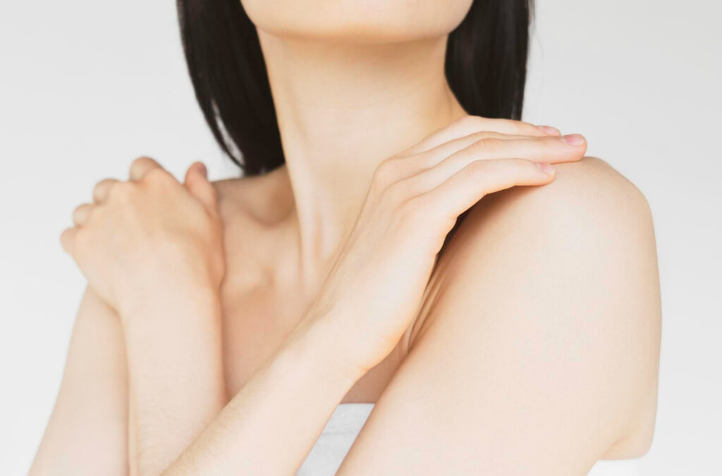 Woman with smooth white skin gently placing her hand across her shoulder, showcasing clear and healthy skin.