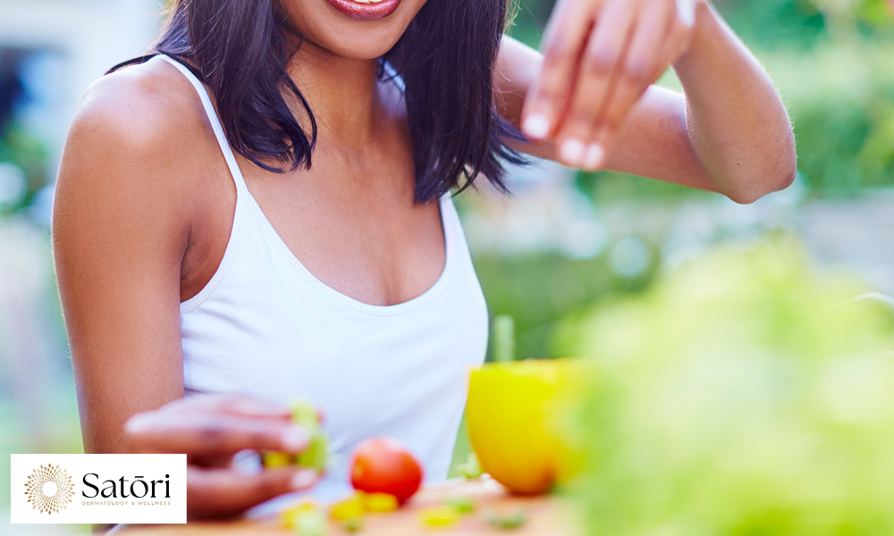 Smiling woman sitting at a table, eating a plate of healthy food including vegetables and lean protein.